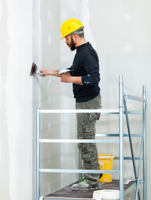 Interior construction, worker plastering gypsum board wall.